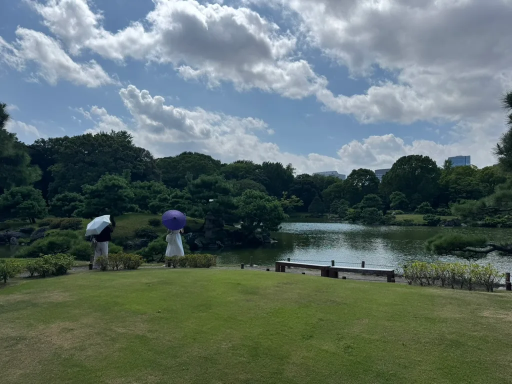 青空の下に池と緑が広がり、和傘を差して散策できる清澄庭園