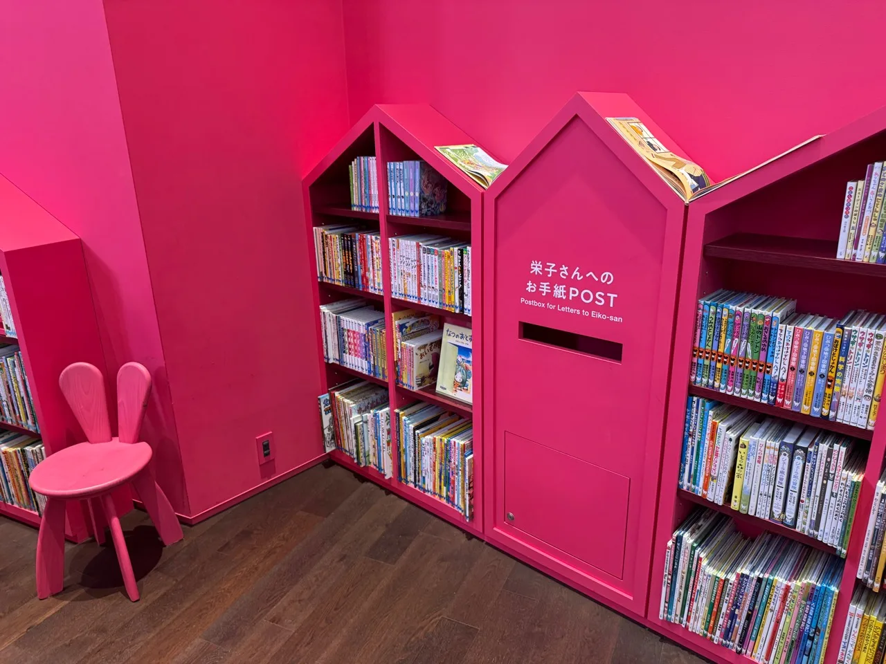 魔法の文学館の家の形をしたピンクの本棚と子ども用の椅子