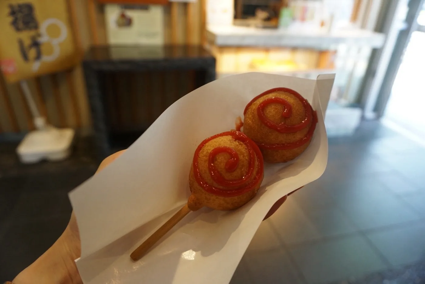 紙に包まれ、ケチャップがかかったひょうたん揚げを手に持っているところ